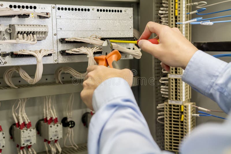 Destornillador y cortaalambres en manos del electricista contra la caja eléctrica con el terminal, los alambres y los reguladores fotos de archivo libres de regalías Destornillador y cortaalambres en manos del electricista contra la caja eléctrica con el terminal, los alambres y los reguladores fotos de archivo libres de regalías