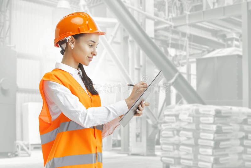 Destroying gender stereotypes. Female builder standing against industrial background. Destroying gender stereotypes. Female builder in orange helmet standing stock photography Destroying gender stereotypes. Female builder standing against industrial background. Destroying gender stereotypes. Female builder in orange helmet standing stock photography