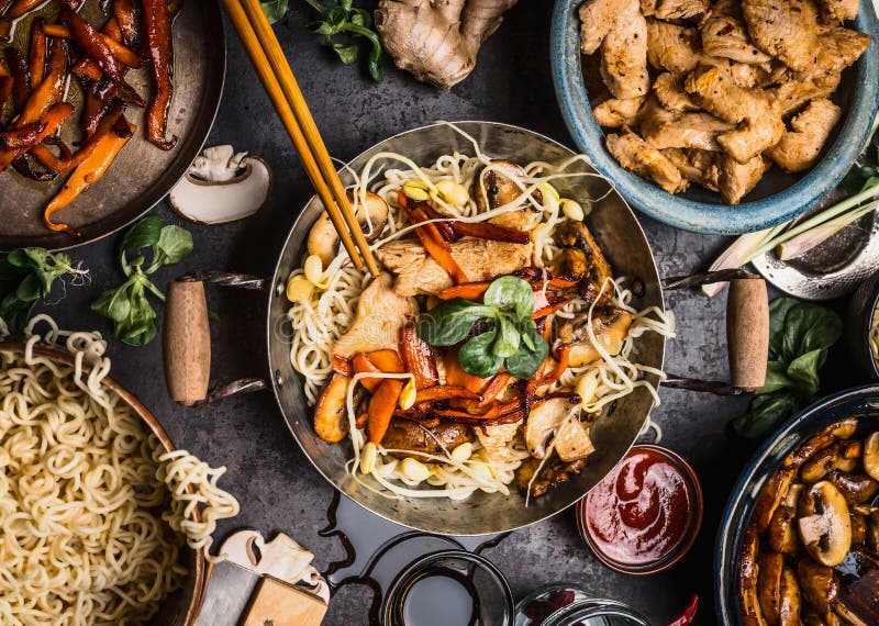 Det asiatiska köksbordet med matskålar, wokar, uppståndelsesmåfisk, pinnar och ingredienser på bakgrund arkivbild Det asiatiska köksbordet med matskålar, wokar, uppståndelsesmåfisk, pinnar och ingredienser på bakgrund arkivbild