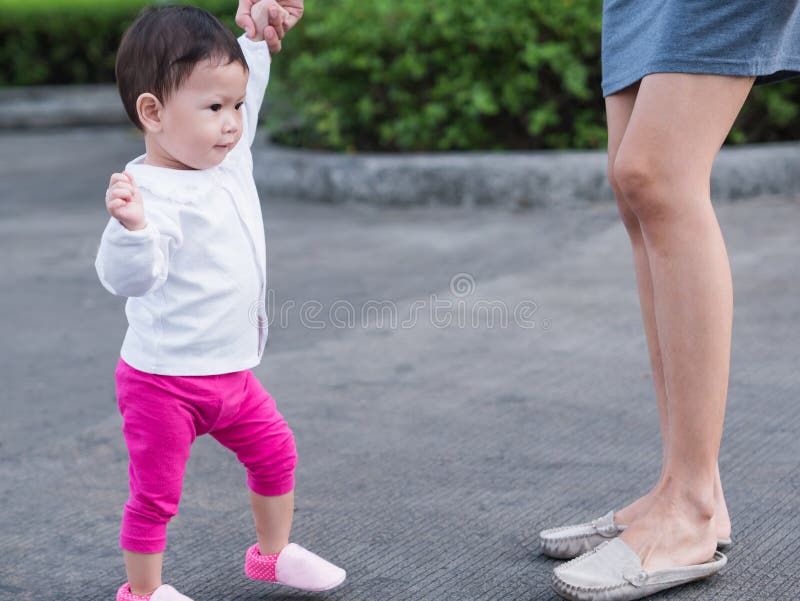 Det asiatiska lilla barnet lär till att gå som är utomhus- Hand för moderhålldaugther royaltyfri bild Det asiatiska lilla barnet lär till att gå som är utomhus- Hand för moderhålldaugther royaltyfri bild
