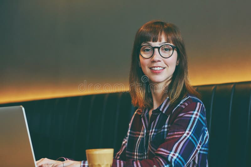 Det här kaféet får bara mina kreativa idéer att flöda. Bild av en attraktiv ung kvinna som använder sin bärbara dator i ett kafé. arkivbild