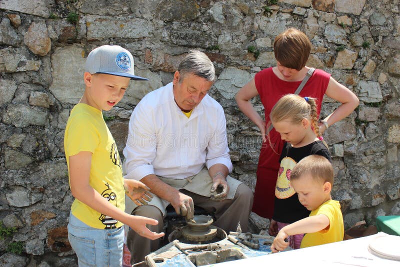 Det idérika seminariet av traditionellt handcrafts - keramikern undervisar barn hur man gör krukmakeri på potterÂs hjul arkivbild Det idérika seminariet av traditionellt handcrafts - keramikern undervisar barn hur man gör krukmakeri på potterÂs hjul arkivbild