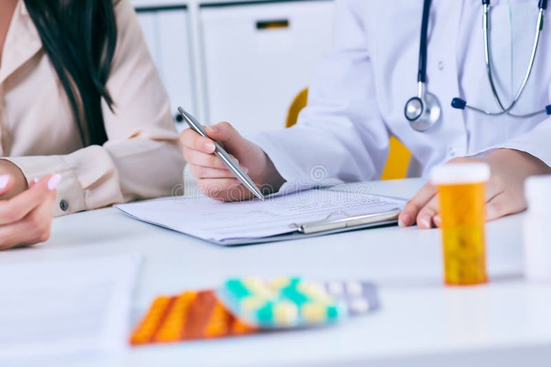 Det kvinnliga doktorsmötet med en patient i kontoret, ger hon ett recept till kvinnan Precis händer över tabellen royaltyfri foto Det kvinnliga doktorsmötet med en patient i kontoret, ger hon ett recept till kvinnan Precis händer över tabellen royaltyfri foto