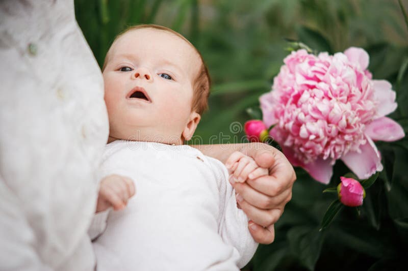 Det nyfödda barnet i moderhänderna finns nära blommor i trädgården. Kärleksvård och familj på landsbygden. Glad royaltyfri bild