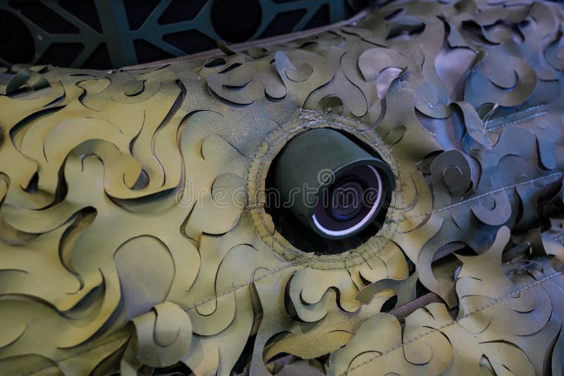 Detail on camera lens mounted at heavy armoured military vehicle covered with camouflage mesh royalty free stock photography