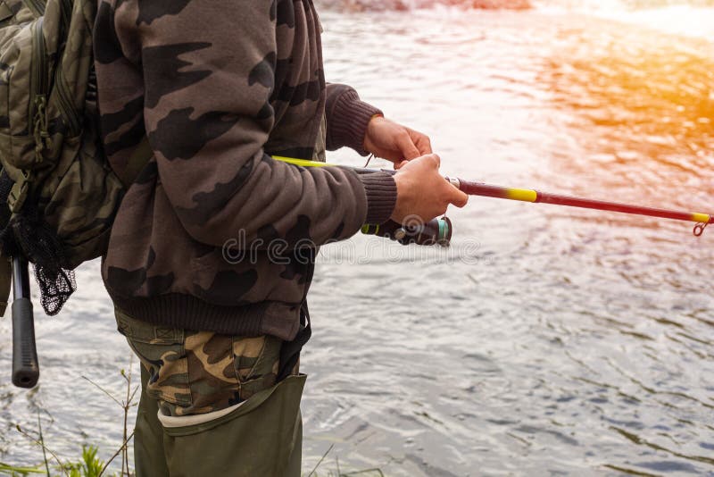 Detail of a fisherman in camouflage clothing high rubber boots holding a rod for fishing in the river with copy space stock images