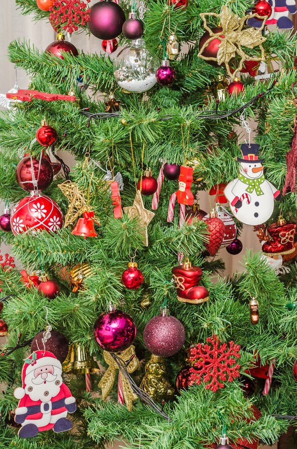 Detail of green Christmas tree with colored ornaments, globes, stars, Santa Claus, Snowman, red boots, shoes, candles