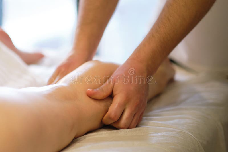 Detail of hands massaging human calf muscle.Therapist applying pressure on female leg. Hands of massage therapist. Massaging legs of young woman in spa salon