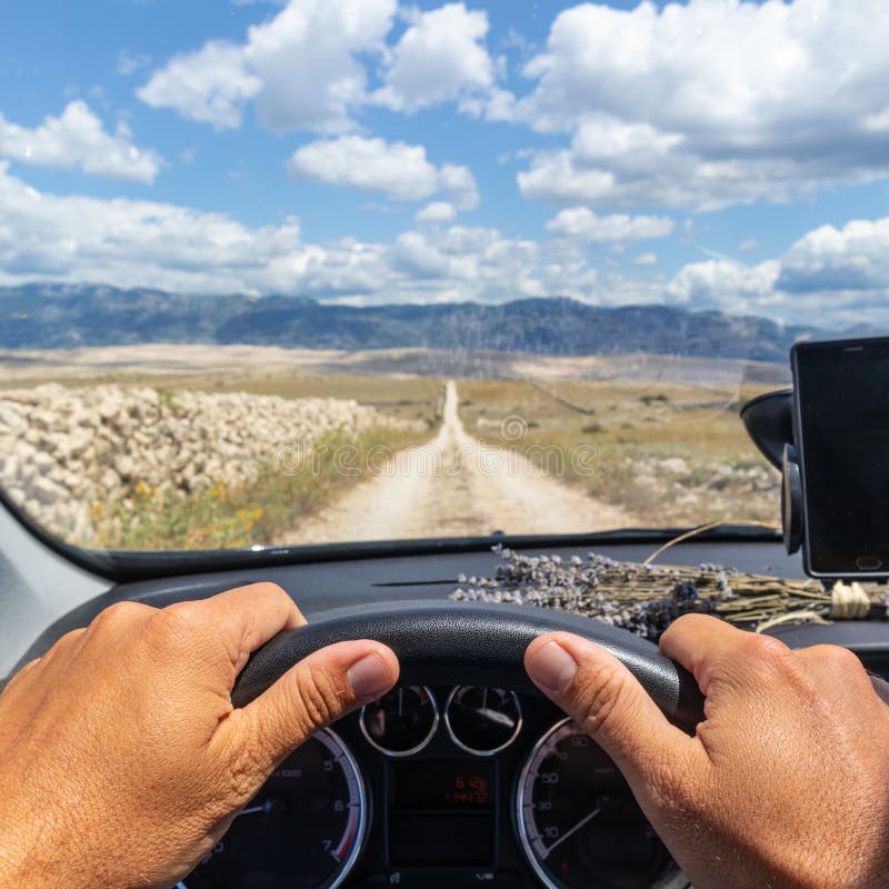 Detail of male driver hands on steering wheel. Driving a car on country road. View from the cabin trough the windshield.