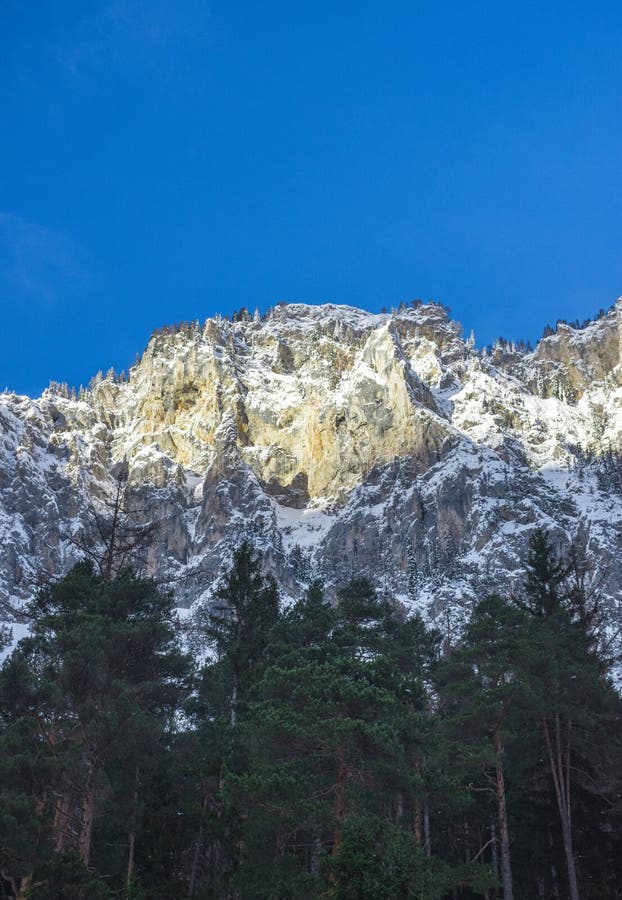 Detail of mountain face with rocks, snow and trees near Green lake Grunner see in sunny winter day. Famous tourist destination