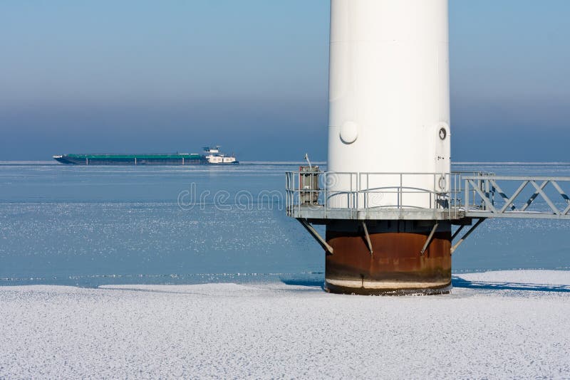 Detail of an offshore windturbine in a frozen sea, A freighter ship is passing