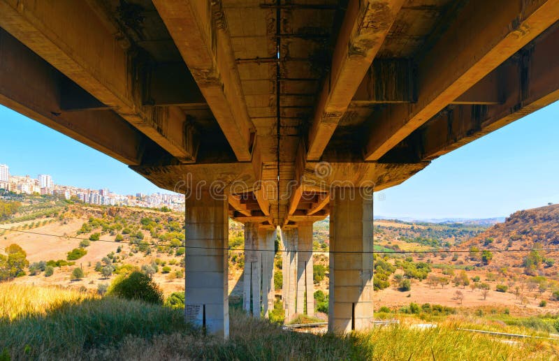 Detail of Ponte Morandi bridge structure with city of Agrigento in background on hill.