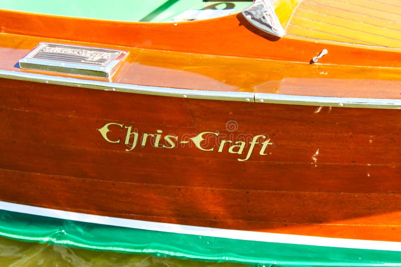 Detail of side of a classic wood Chris-Craft boat with logo painted on wood and water lapping bottom visible at bottom