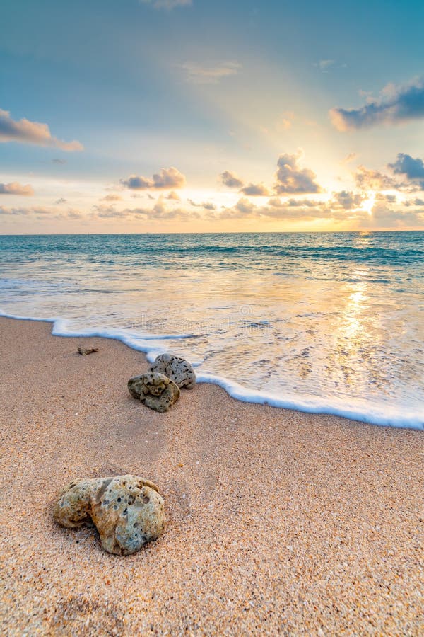 Detail view of rock on the beach, placed in the sand, with big water wave from the sea. Beautiful sunset above ocean with soft