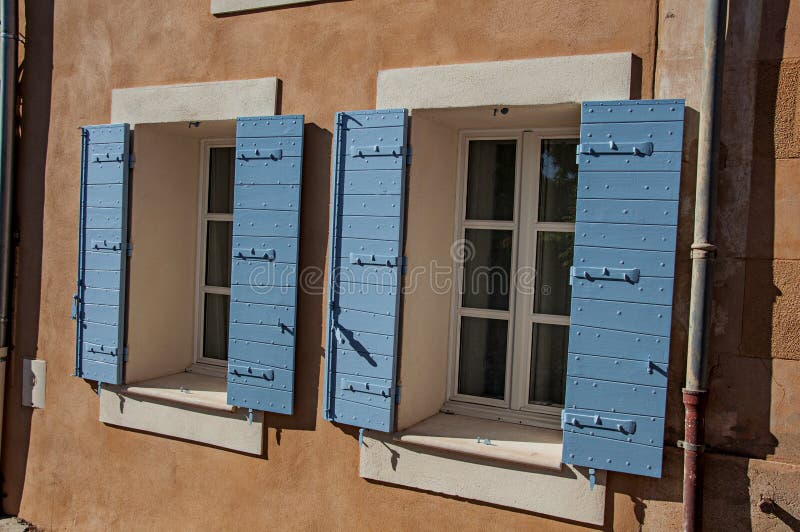 Roussillon, France - July 03, 2016. Detail of windows with blue shutters at sunset in the city center of the village of Roussillon. In the Vaucluse department, Provence region, in southeastern France. Roussillon, France - July 03, 2016. Detail of windows with blue shutters at sunset in the city center of the village of Roussillon. In the Vaucluse department, Provence region, in southeastern France