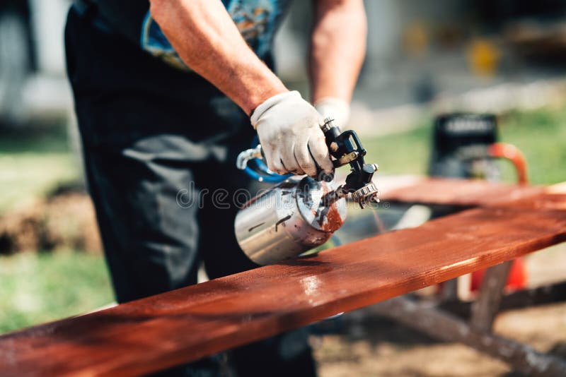 Details of man using spray gun or airbrush for painting fence. Carpentry details with woodwork and handyman