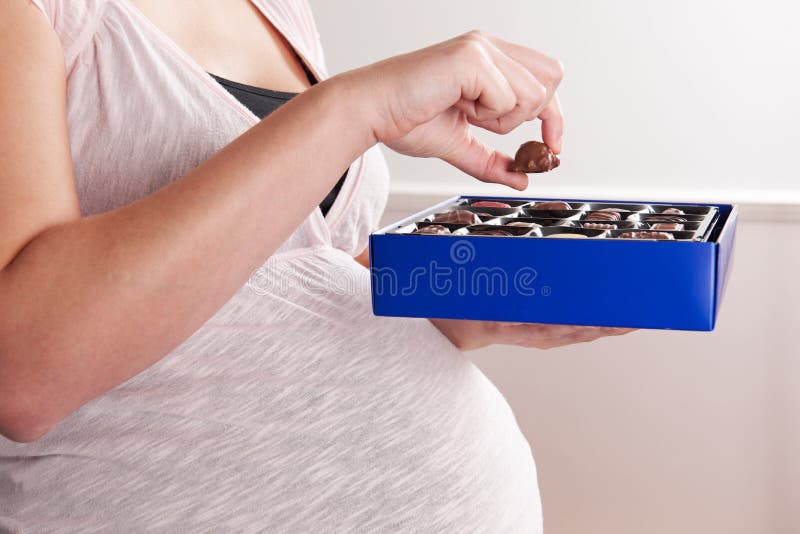 Detalle de la mujer embarazada que come la caja de chocolates imagen de archivo libre de regalías Detalle de la mujer embarazada que come la caja de chocolates imagen de archivo libre de regalías
