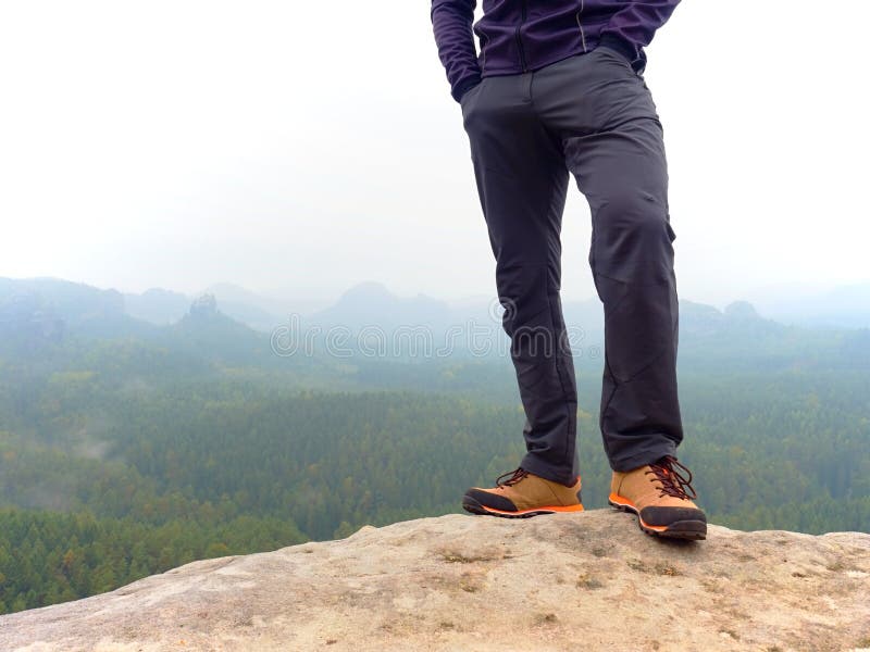 Vista de las piernas y botas del hombre sobre una roca en la cima de la  montaña con vistas a un valle