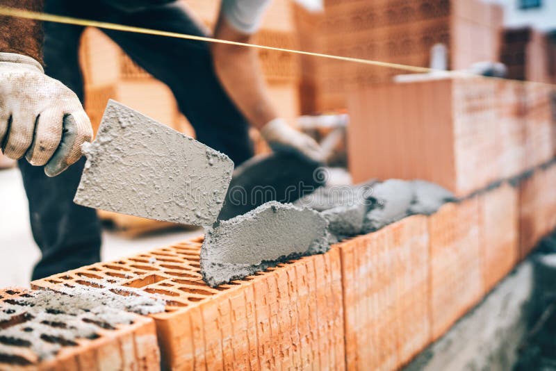 Detalles del trabajador de construcción, engranaje protector y paleta con las paredes de ladrillo del edificio del mortero