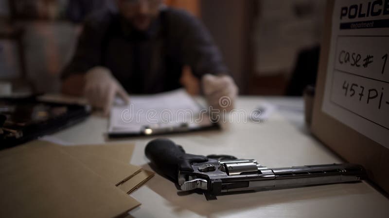 Detective del hombre que examina el arma del revólver y que llena la investigación del informe de la experiencia fotos de archivo libres de regalías Detective del hombre que examina el arma del revólver y que llena la investigación del informe de la experiencia fotos de archivo libres de regalías