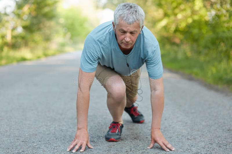 Determined elederly strong male participates in marathon races, ready to run, dressed in sportswear, supports healthy lifestyle, l royalty free stock photo Determined elederly strong male participates in marathon races, ready to run, dressed in sportswear, supports healthy lifestyle, l royalty free stock photo