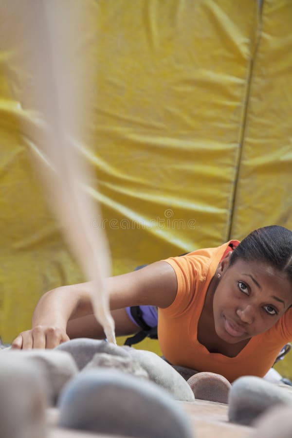 Determined young woman climbing up a climbing wall in an indoor climbing gym, directly above
