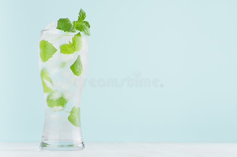 Detoxkallt vatten med gröna mintkaramellsidor, iskuber och uppiggningsmedel i elegant exponeringsglas på den vita trätabellen, mi