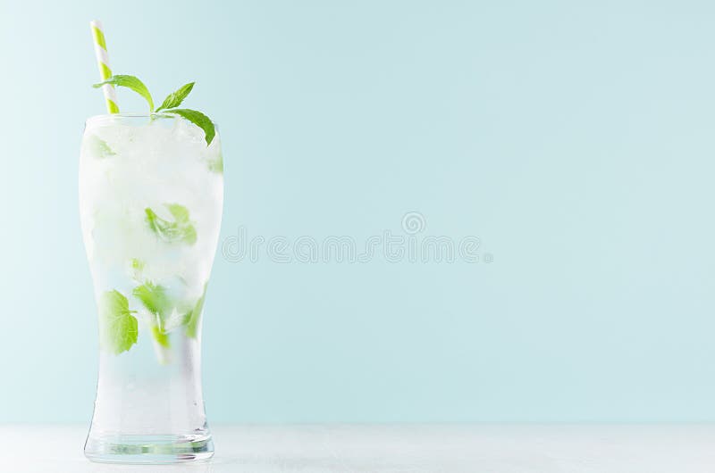 Detoxkallt vatten med gröna mintkaramellsidor, iskuber, randigt sugrör, uppiggningsmedel i elegant exponeringsglas på den vita tr