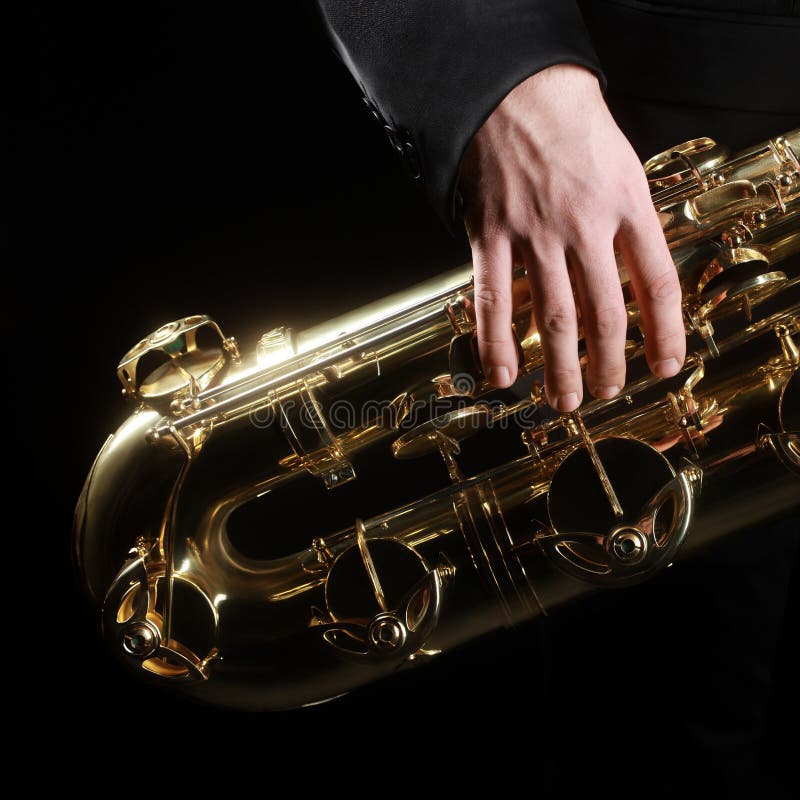Saxophone jazz music instruments details. Baritone sax with hand of saxophonist closeup on black. Saxophone jazz music instruments details. Baritone sax with hand of saxophonist closeup on black