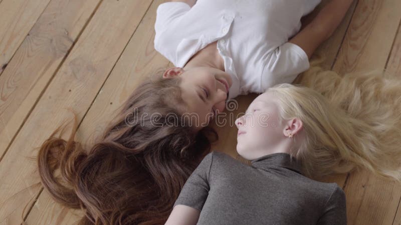 Deux amies se trouvant sur le plancher en bois regardant l'un l'autre Concept de l'amiti? Enfance insouciant Gens r?els