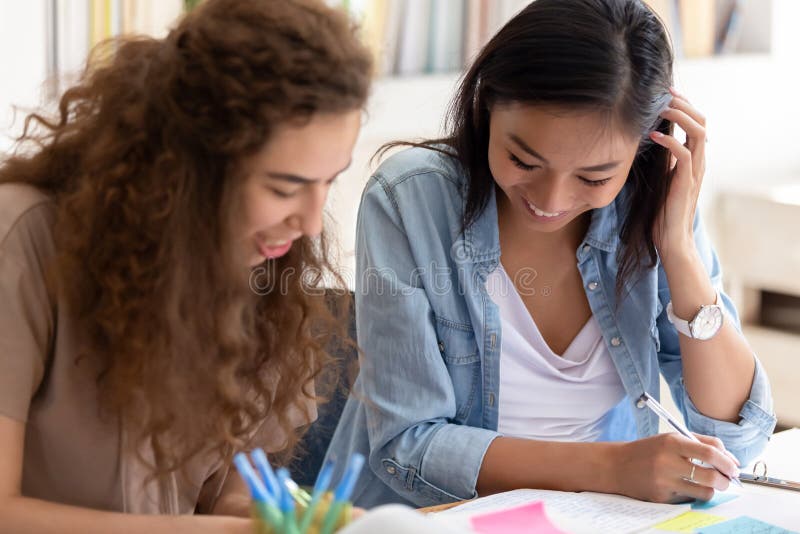 Two happy diverse girls college friends study together in campus, teen asian and caucasian female students team talking laughing helping in preparing university creative research project make notes. Two happy diverse girls college friends study together in campus, teen asian and caucasian female students team talking laughing helping in preparing university creative research project make notes