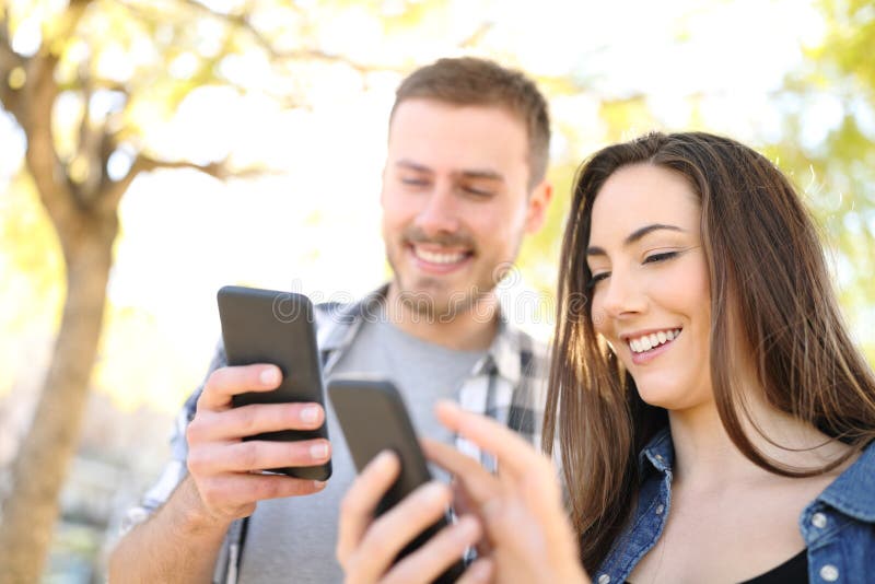 Deux amis heureux à l'aide de leurs téléphones intelligents dans un parc photographie stock Deux amis heureux à l'aide de leurs téléphones intelligents dans un parc photographie stock