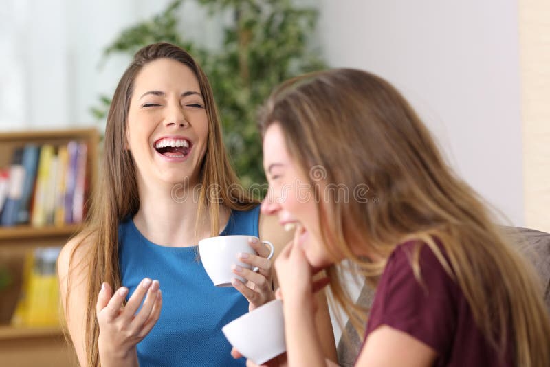 Portrait of two friends laughing loud together during a conversation sitting on a couch in the living room at home. Portrait of two friends laughing loud together during a conversation sitting on a couch in the living room at home