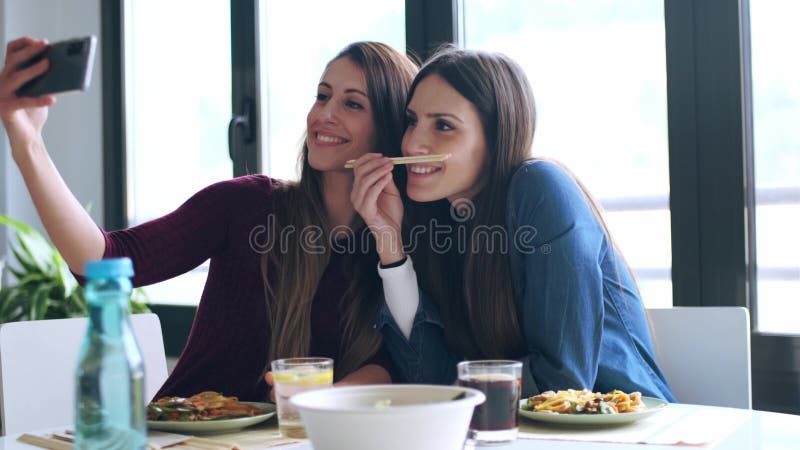 Deux belles amies souriantes mangeant de la nourriture japonaise tout en prenant un selfie avec un téléphone intelligent dans la c clips vidéos