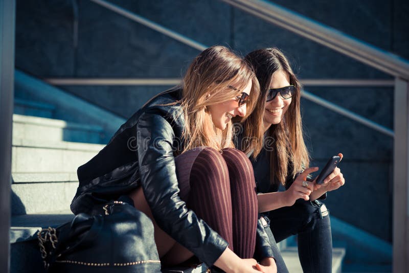 Deux belles jeunes femmes à l'aide du téléphone intelligent photographie stock libre de droits Deux belles jeunes femmes à l'aide du téléphone intelligent photographie stock libre de droits