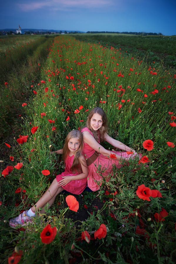Deux belles jeunes soeurs marchant dans le domaine de pavot photographie stock Deux belles jeunes soeurs marchant dans le domaine de pavot photographie stock