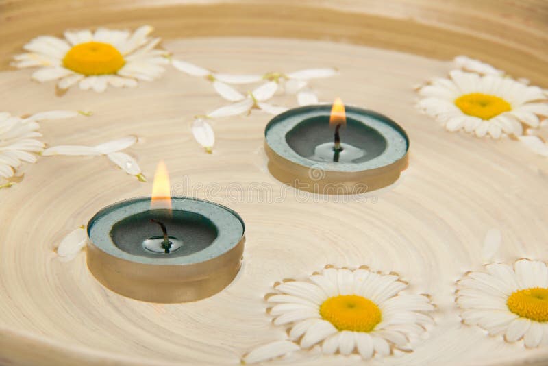 Two burning candles, heads of camomiles in a dish with water. Two burning candles, heads of camomiles in a dish with water