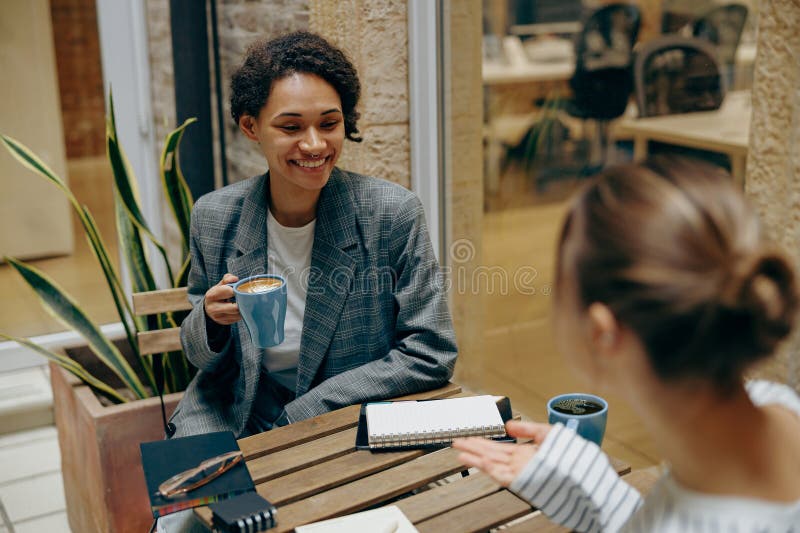 Smiling female coworkers talking and drink coffee while have a break time sitting in cafe. Smiling female coworkers talking and drink coffee while have a break time sitting in cafe