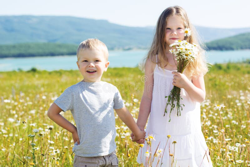 Two cute friends girl and boy are playing at camomile field, summer time. Two cute friends girl and boy are playing at camomile field, summer time