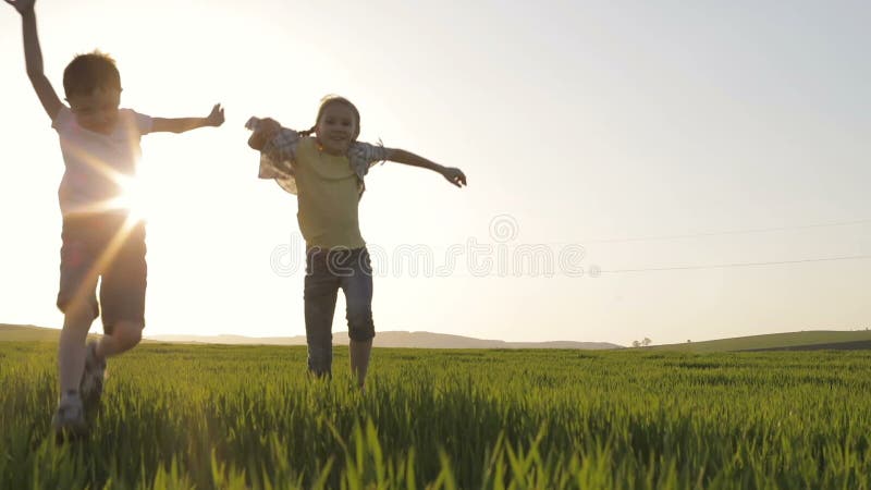 Deux enfants heureux jouant dans le domaine au temps de coucher du soleil