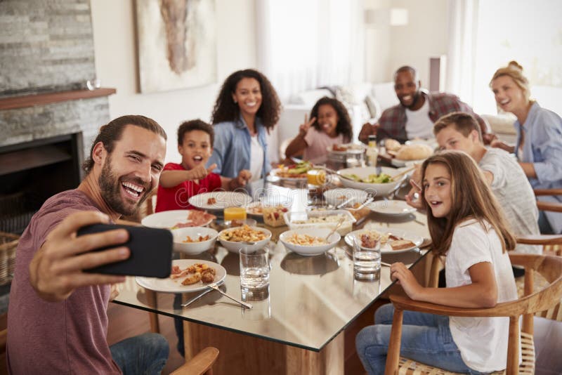 Deux familles prenant Selfie comme elles apprécient le repas à la maison ensemble photos stock Deux familles prenant Selfie comme elles apprécient le repas à la maison ensemble photos stock
