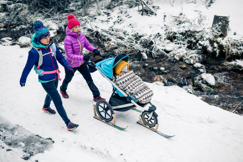 Deux femmes avec le promeneur de bébé appréciant l'hiver dans la forêt, temps de famille image libre de droits Deux femmes avec le promeneur de bébé appréciant l'hiver dans la forêt, temps de famille image libre de droits