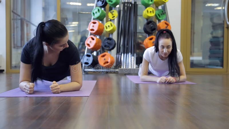 Deux femmes faisant la courroie d'exercice sur ses coudes dans la classe de sport