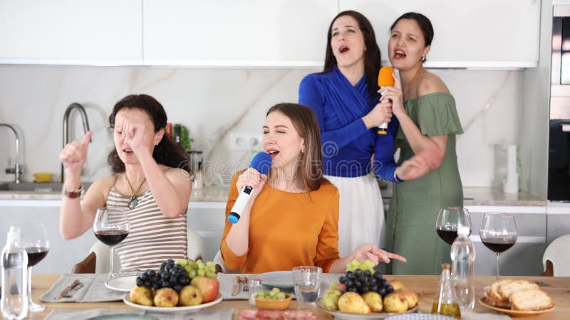 Deux femmes joliment assises à table fixe avec du vin et des fruits chantant dans des microphones lors d'une séance de karaoké ani clips vidéos
