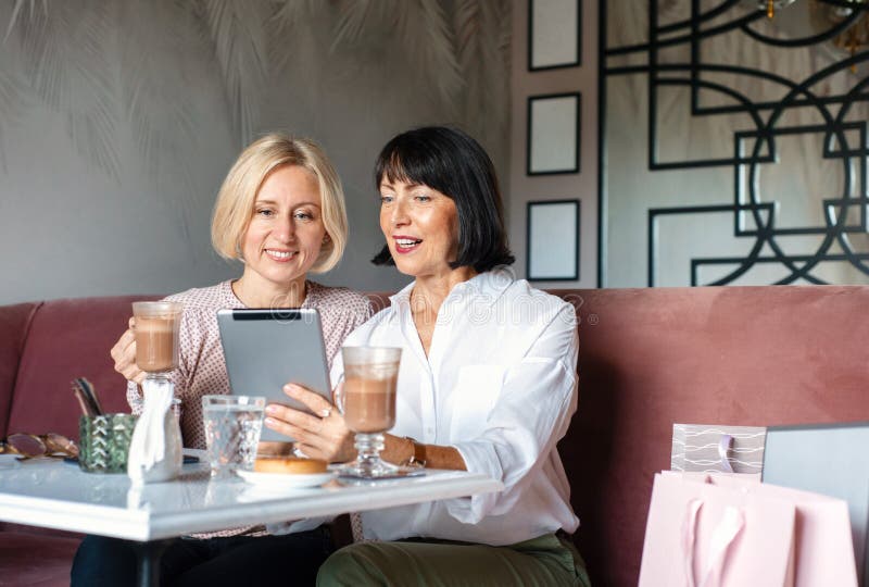 Deux femmes matures bavarder et utiliser le dispositif de la tablette tout en déjeunant dans un café photographie stock libre de droits