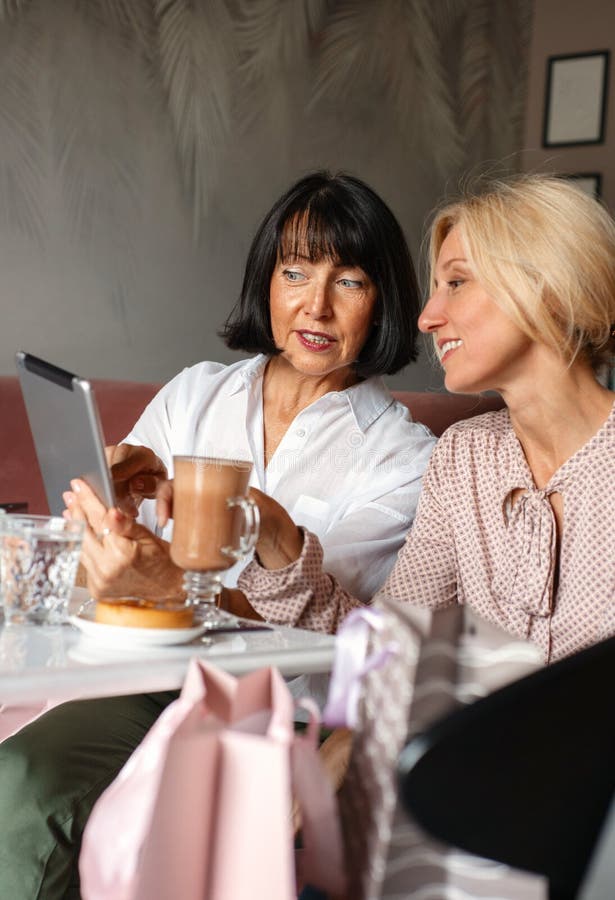 Deux femmes matures bavarder et utiliser le dispositif de la tablette tout en déjeunant dans un café photos stock