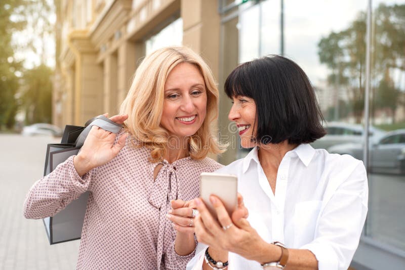 Deux femmes matures regardant le téléphone et s'amusant en faisant des courses photo stock