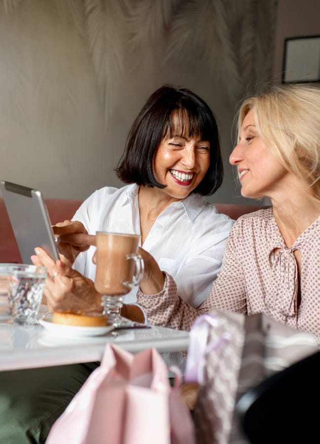 Deux femmes matures qui discutent et utilisent l'appareil de la tablette pendant qu'elles déjeunent au café photos stock