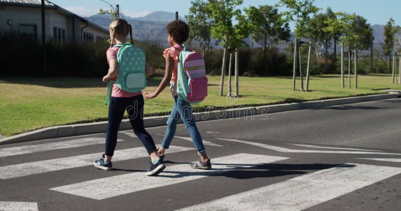 Deux filles avec des sacs d'école traversant la route banque de vidéos