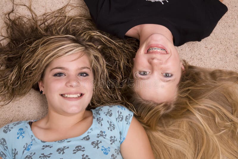 Two teenage girls laying together with their heads together smiling. Two teenage girls laying together with their heads together smiling.